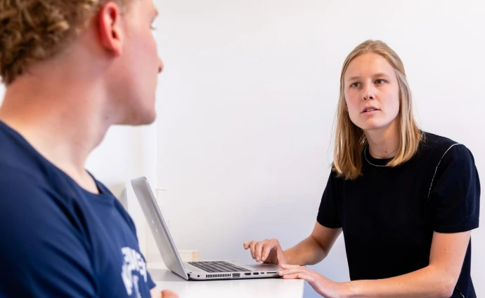 Twee mensen praten naast een laptop aan een tafel.