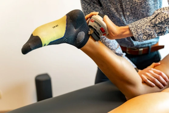 Een fysiotherapeut behandelt een gebogen been met een massageapparaat.