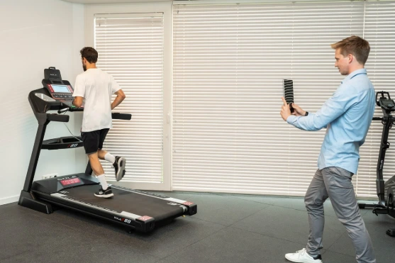 Een man rent op een loopband terwijl een andere man hem met een smartphone filmt.