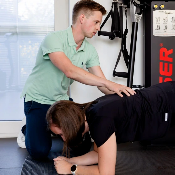 Een man ondersteunt een vrouw tijdens een oefening op een fitnessmat.