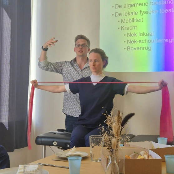 Een vrouw doet een oefening met een elastische band terwijl een man uitleg geeft tijdens een presentatie.