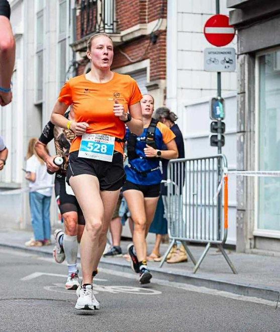 Twee hardlopers rennen over een blauwe strook, terwijl dranghekken en publiek langs het parcours staan.