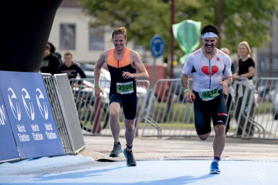 Twee mannen trainen met een halter; één voert een squat uit terwijl de ander toekijkt.