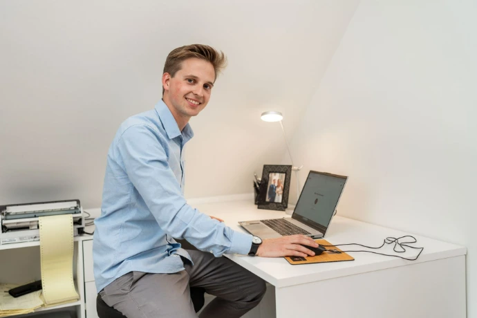 Jonge man werkt aan een laptop aan een wit bureau.