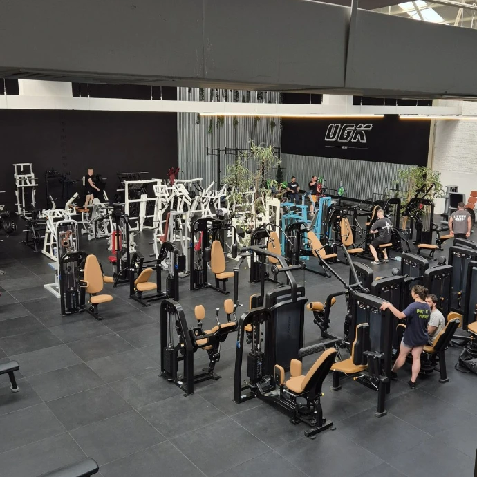 Ruime sportschool met talrijke fitnessapparaten en enkele sportende mensen.